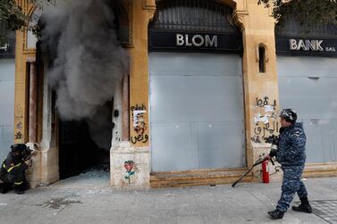A firefighter looks before entering a bank that was set on fire by anti-government protesters, as a riot policeman passes by, during a protest in downtown Beirut. AP