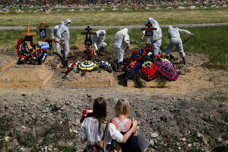 Mourners watch grave diggers burying a person who died of Covid-19 in the special purpose section of a graveyard on the outskirts of Saint Petersburg, Russia.  Reuters