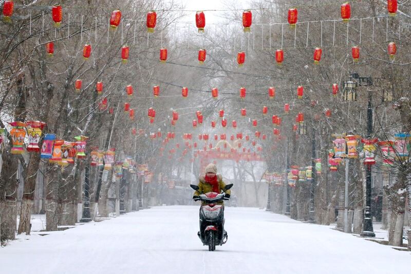 A woman rides a motorcycle past a snow-covered street decorated with lanterns, ahead of the Chinese Lunar New Year, in Zhangye, Gansu province, China.  Reuters