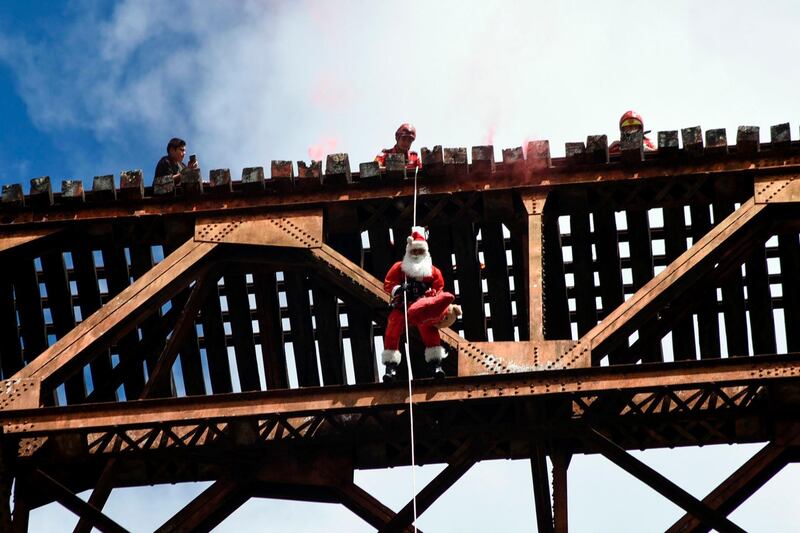 Guatemalan municipal firefighter Hector Chacon, dressed as Santa Claus, goes down a cable from a bridge to deliver presents to children in Guatemala City.   AFP