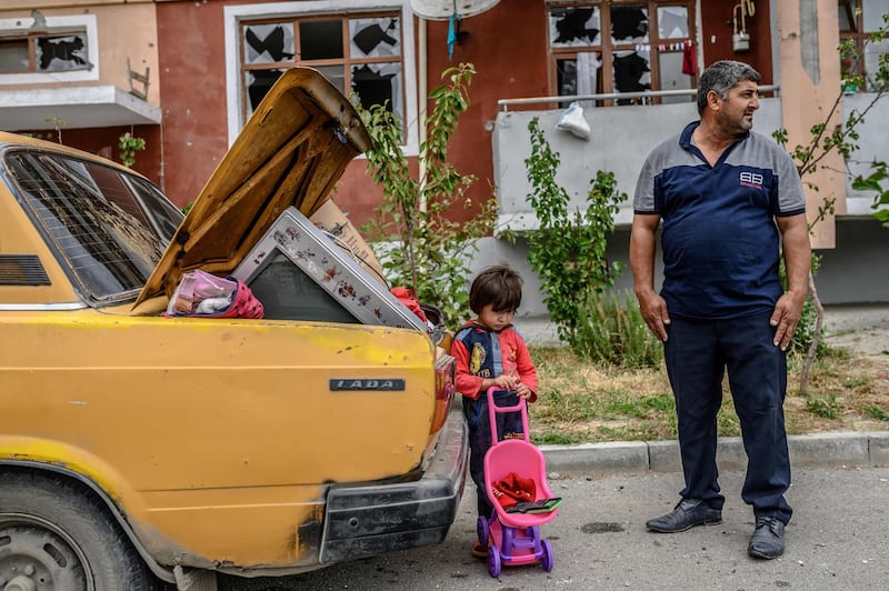 Father and child by a car outside a damaged apartment building after the family took their last belongings from their flat during a ceasefire during a military conflict between Armenia and Azerbaijan over the breakaway region of Nagorno-Karabakh, in the town of Terter, Azerbaijan, on October 10. Bulent Kilic / AFP