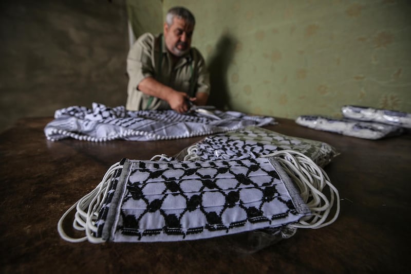 Nabil Saber Abu Ghabin cuts up the checkered cotton cloth he normally uses to make the traditional Palestinian keffiyeh into a facemask at his workshop in Gaza City.  EPA