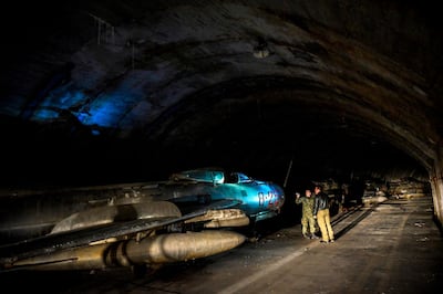 Albanian military personnel walk next to MIG-19 jet fighters inside the main tunnel of the Gjader Air Base built near the city of Lezhe, on February 5, 2019. On a barren hillside in northern Albania lies a portal to the country's communist past: a massive steel door creaks open to reveal a hidden former air base burrowed into the heart of the mountain. Made up of 600 metres (1,980 feet) of tunnels that once teemed with military life, the secret Gjader air base is now a depot for dozens of hulking communist-era MiG jets collecting dust in the darkness. Three decades after shedding communism, Albanian authorities are still trying to sell off the Soviet and Chinese-made aircraft, of which there are dozens more in another nearby air base.
 / AFP / Gent SHKULLAKU
