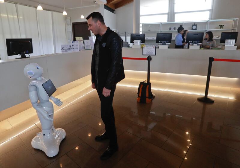 Mihail Slanina, a guest from Moldavia, askst robot Robby Pepper for information at the front desk of hotel in Peschiera del Garda, northern Italy, Monday, March 12, 2018. Robby Pepper, billed as Italyâ€™s first robot concierge, has been programed to answer simple guest questions in Italian, English and German, the humanoid, speaking robot will be deployed all season at a hotel on the popular Garda Lake to help relieve the desk staff of simple, repetitive questions. (AP Photo/Luca Bruno)