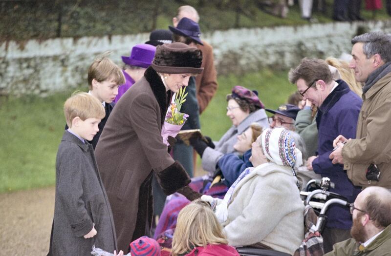 British Royals Prince Harry, Prince William and Diana, Princess of Wales (1961-1997), wearing a brown coat with black trim and a matching winter hat, greeting wellwishers as they attend the Christmas Day service at St Mary Magdalene Church on the Sandringham Estate in Sandringham, Norfolk, England, 25th December 1994. Partially obscured in the background are Queen Elizabeth II and Prince Philip. (Photo by Princess Diana Archive/Hulton Archive/Getty Images)