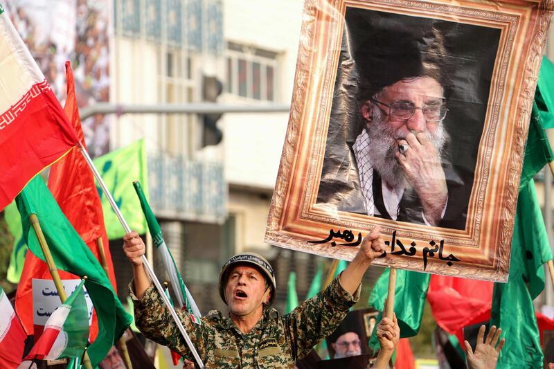 TOPSHOT - A man dressed in a military uniform chants slogans as Iranian pro-government demonstrators raise national flags and a picture of the Islamic republic's supreme leader, Ayatollah Ali Khamenei, during a rally in the capital Tehran's central Enghelab Square on November 25, 2019, to condemn days of "rioting" that Iran blames on its foreign foes. In a shock announcement 10 days ago, Iran had raised the price of petrol by up to 200 percent, triggering nationwide protests in a country whose economy has been battered by US sanctions. / AFP / ATTA KENARE
