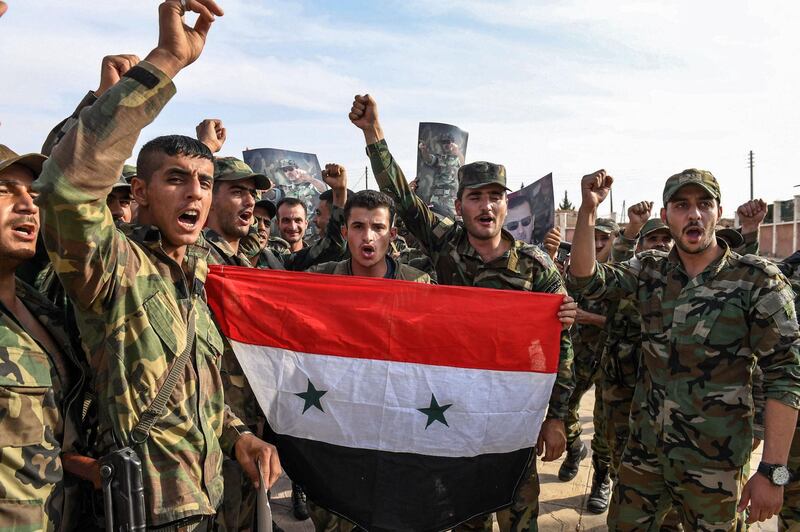 Syrian government soldiers chant slogans as they pose for a group photo with a national flag and portraits of President Bashar al-Assad near the outskirts of the northern city of Manbij in the north of Aleppo province as government forces deploy there on October 15, 2019.  / AFP / -
