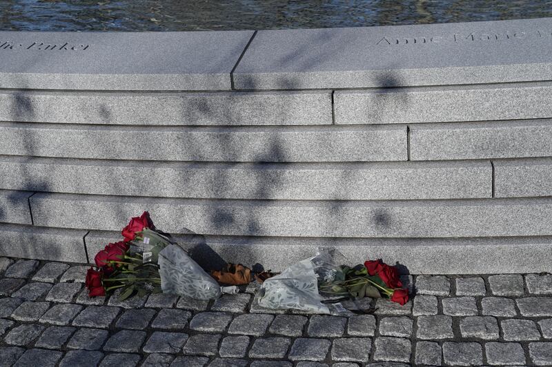 Flowers lie on the cobblestones at the foot of the memorial. The National