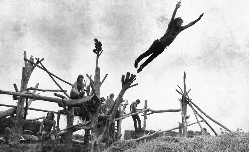 Fans sit on a tree sculpture as one leaps mid-air onto a pile of hay during the Woodstock Music Festival. AP Photo