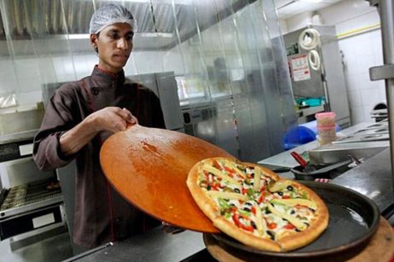 A cook slides a pizza onto a serving plate in the kitchen at a Pizza Hut restaurant in Mumbai, March 29, 2011. A number of fast-food and cafe chains that are flocking to India would do well to take away lessons learned by established rivals such as McDonald's in navigating a market beset with obstacles. Industry experts say patience and flexibility in a country where dietary traditions rule may well define successful global restaurant brands in India. The stakes are high, with India's quick-service restaurant market worth $13 billion and growing roughly 25-30 percent a year, according to Euromonitor and market research firm RNCOS. India's entire food-service market is estimated at $64 billion.  Picture taken March 29, 2011. To match analysis INDIA-FASTFOOD/      REUTERS/Danish Siddiqui (INDIA - Tags: BUSINESS FOOD)