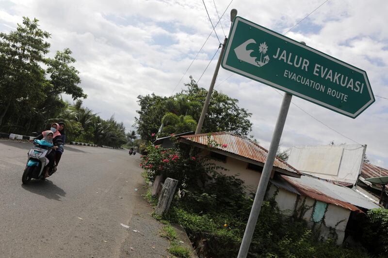 A woman rides a motorbike past a sign pointing at a tsunami evacuation route in Banda Aceh, Indonesia. EPA
