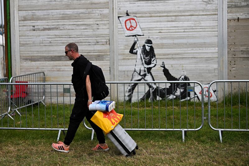 A Reveller walks by a graffiti attributed to Banksy as he arrives at Worthy Farm in Somerset during the Glastonbury Festival in June 2022. Reuters