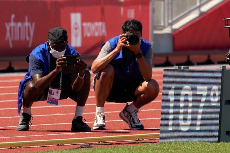 Photographers take pictures of an onfield sign displaying the current temperature after events were postponed due to high heat at the U.S. Olympic Track and Field Trials Sunday, June 27, 2021, in Eugene, Ore. (AP Photo/Charlie Riedel)