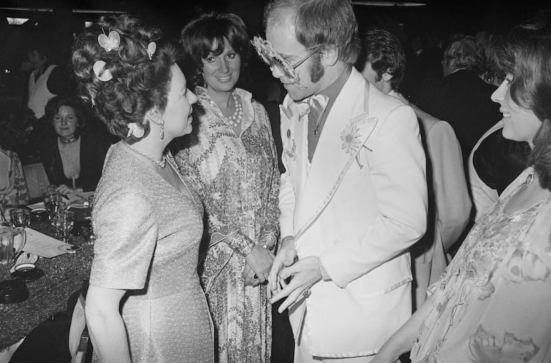 Princess Margaret speaks to Elton John, wearing a white suit with a daisy on his lapel, at an event in 1974. Getty Images