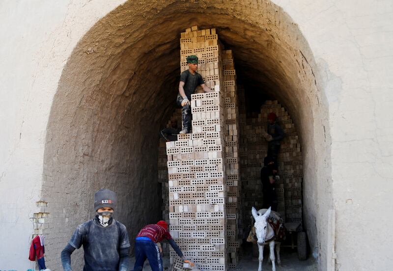 Men stack bricks at the factory, as a donkey harnessed to a cart waits below.
