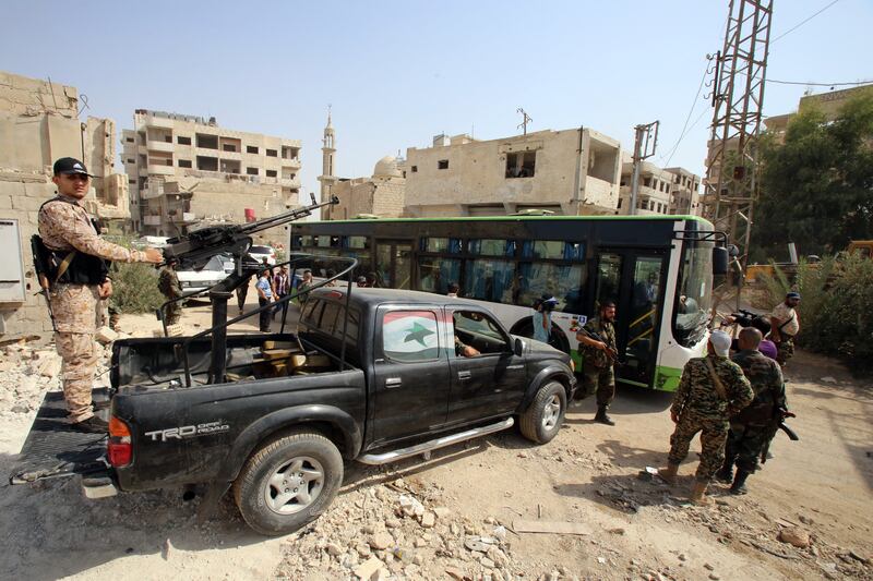 Syrian government troops on guard as a bus drives by with people from the evacuated town of Daraya outside the capital Damascus on August 26, 2016. The move was part of a deal agreed between the government and opposition fighters after a four-year army siege. AFP