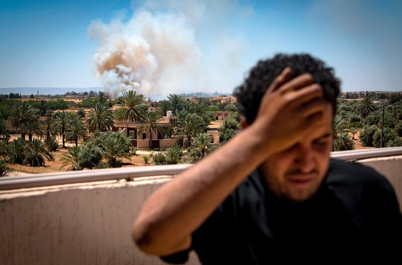 A fighter loyal to the internationally-recognised Government of National Accord (GNA) stands on a rooftop as smoke rises in the distance during clashes with forces loyal to strongman Khalifa Haftar, in Espiaa, about 40 kilometres (25 miles) south of the Libyan capital Tripoli on April 29, 2019.  Fierce fighting for control of Libya's capital that has already displaced tens of thousands of people threatens to bring a further worsening of humanitarian conditions, a senior UN official has warned. / AFP / Fadel SENNA
