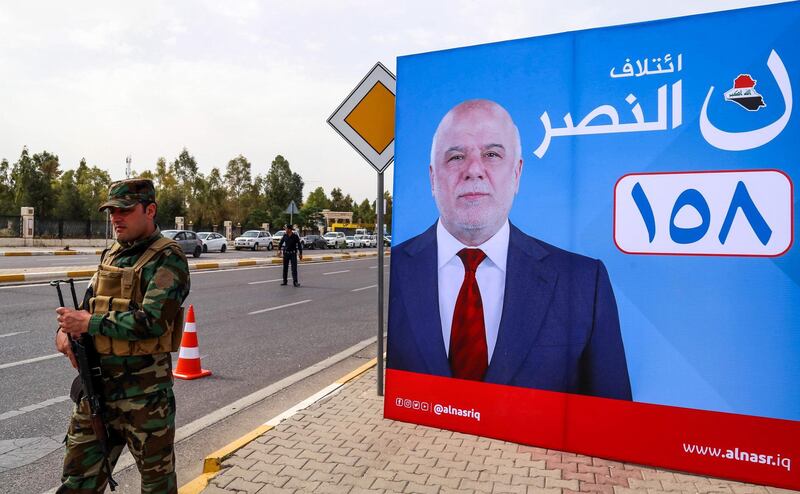 A member of Kurdish security stands near a campaign banner for Iraqi Prime Minister Haider al-Abadi, for the upcoming parliamentary elections in the capital of the northern Iraqi Kurdish autonomous region Arbil on April 26, 2018. / AFP PHOTO / SAFIN HAMED