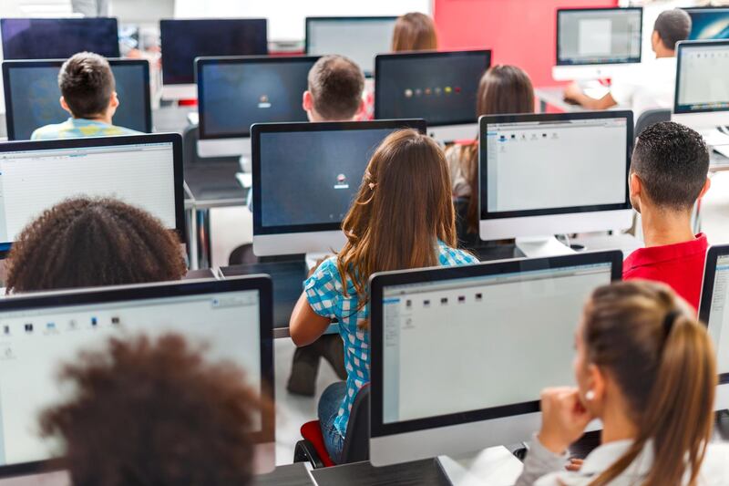 Rear view of large group of people sitting at a computer class and using computers.