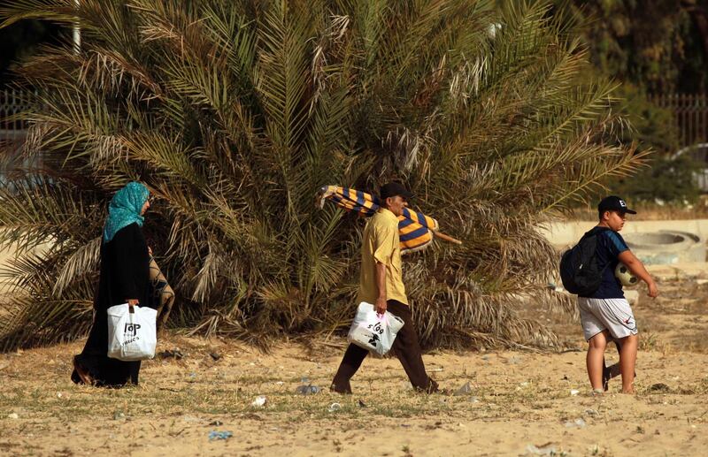 People carrying bags and an umbrella arrive at the beach, along the coast of the eastern Libyan port city of Benghazi on June 20, 2020.  / AFP / Abdullah DOMA
