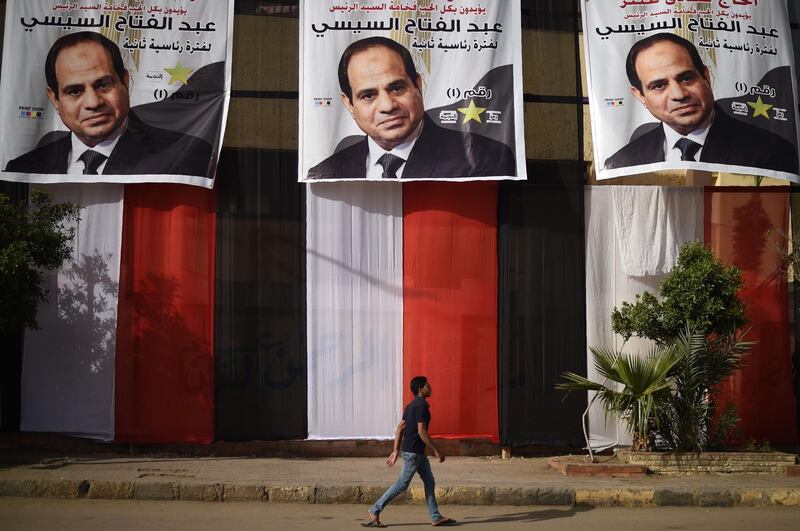 An Egyptian youth walks past a polling station in the capital Cairo's western Giza district on March 25, 2018 ahead of the vote scheduled to begin the following day, decorated on the outside with giant privately-sponsored electoral posters depicting incumbent President Abdel Fattah al-Sisi and giant pieces of cloth stacked together to show the colours of the Egyptian flag. Mohamed El-Shahed / AFP