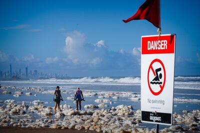 Tourists walk amongst beach foam in the wake of cyclonic conditions at Currumbin Beach on December 15, 2020, after wild weather lashed Australia's Northern New South Wales and South East Queensland with heavy rain, strong winds and king tides. / AFP / AFP  / Patrick HAMILTON
