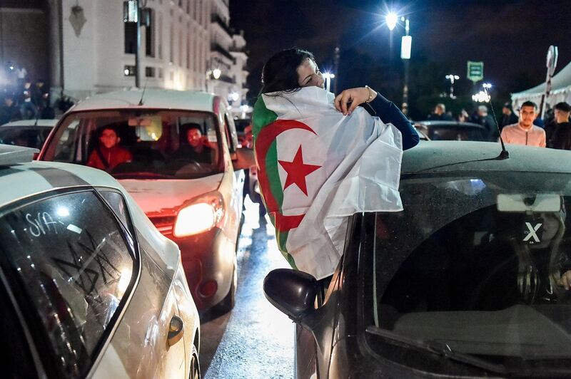 An Algerian woman draped in a national flag sits out from the window of a car during demonstrations in the centre of the capital Algiers on March 11, 2019, after President Abdelaziz Bouteflika announced his withdrawal from a bid to win another term in office and postponed an April 18 election, following weeks of protests against his candidacy.  Bouteflika, in a message carried by national news agency APS, said the presidential poll would follow a national conference on political and constitutional reform to be drawn up by the end of 2019. / AFP / RYAD KRAMDI                        
