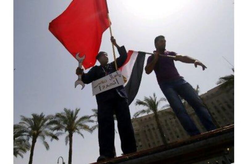 An Egyptian worker holds a red flag of the Egyptian workers union and a banner that reads in Arabic, "workers of Egypt, unite,". Khalil Hamra / AP Photo