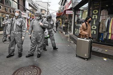 A woman walks past South Korean soldiers wearing protective gear as they spray disinfectant to help prevent the spread of the virus.  AFP 