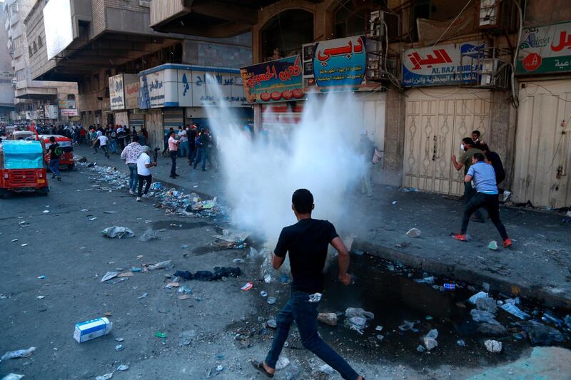 Protesters run for cover while riot police fire tear gas during clashes between Iraqi security forces and anti-government protesters in Baghdad, Iraq. AP Photo