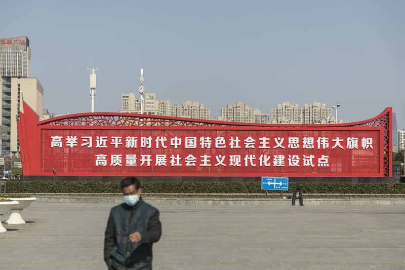 A man wearing a mask walks through a square near a slogan of communist ideology outside the South Railway Station in Shanghai, China, on Sunday, Feb. 2, 2020. Chinese policymakers prepared to shore up the financial system and capital markets, which are bracing for a sell-off on Monday when markets re-open. Photographer: Qilai Shen/Bloomberg
