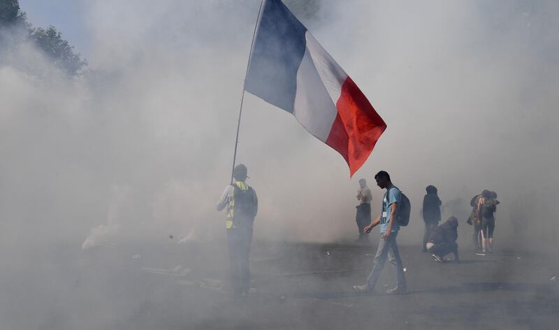 A protester holds a French national flag surrounded by smoke of tear gas during a demonstration called by the "yellow vest" (gilets jaunes) movement in Paris.  AFP