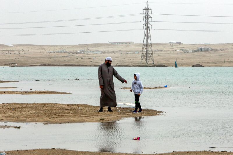 A man and boy walk by a flooded area, caused by heavy rains, in Kuwait's al-Mutlaa desert, about 70 kilometres north of Kuwait City. AFP