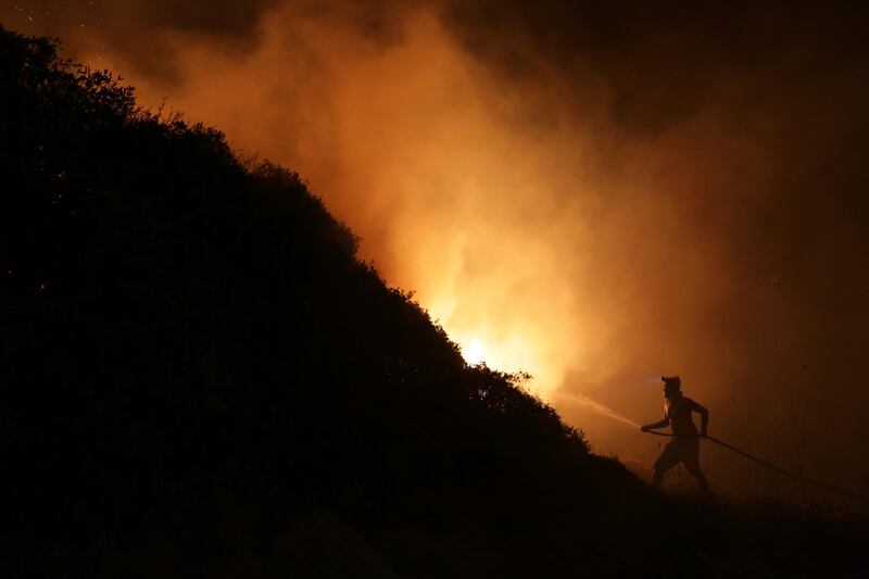 A volunteer uses a water hose to fight a wild fire raging near houses in the outskirts of Obidos, Portugal, in the early hours of Monday, October 16 2017. Armando Franca / AP Photo