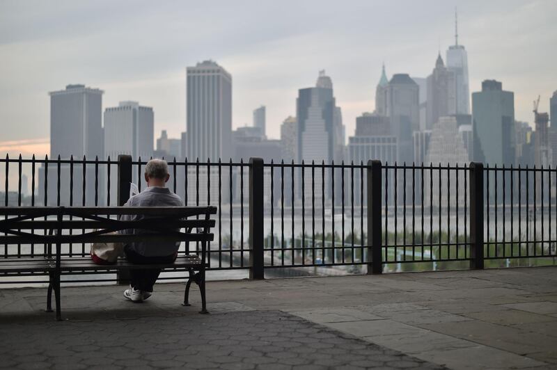 A man sits in the Brooklyn Heights Promenade overlooking the Manhattan skyline, in New York City on May 17, 2018. / AFP / HECTOR RETAMAL
