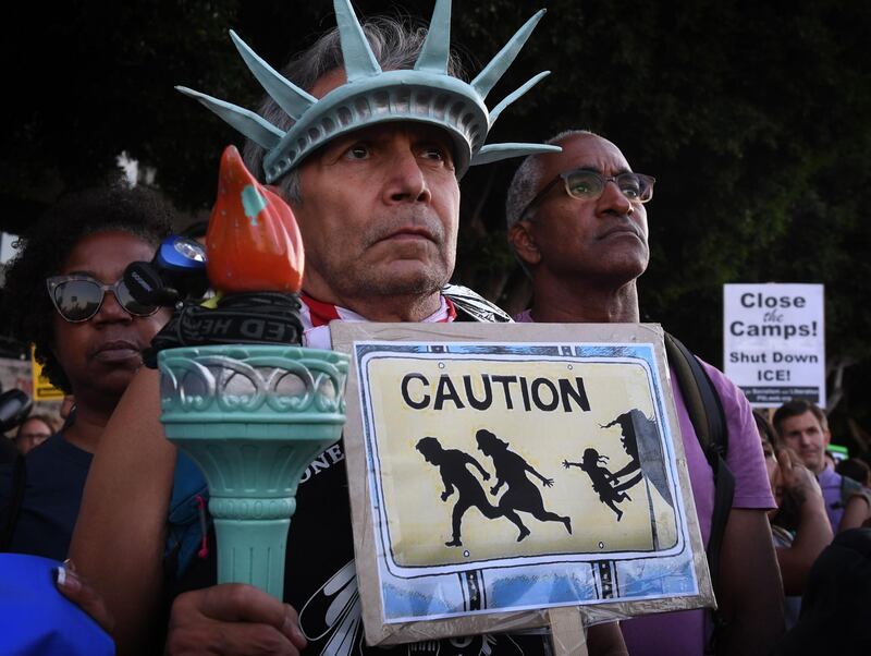 A man wears a Statue of Liberty crown as people protest against the upcoming ICE raids and detentions of refugee asylum seekers at a vigil outside the main ICE detention center in downtown Los Angeles on July 12, 2019.  Numerous vigils were held across the US as part of the Lights for Liberty movement's campaign to call for an end to "inhumane conditions at the border" and the deportations of refugee asylum seekers. / AFP / Mark RALSTON
