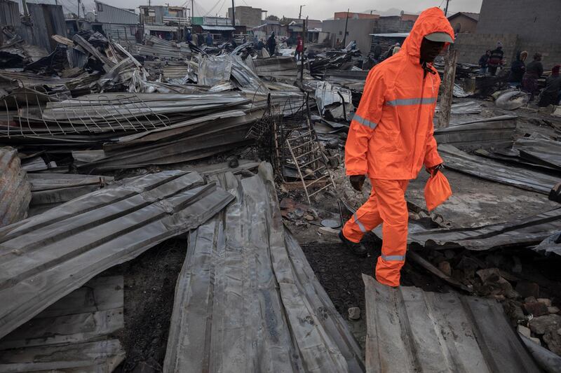 A resident of Masiphumelele informal settlement walks through burned shacks in the rain after a fire destroyed over 250 structures in Masiphumelele, Cape Town, South Africa.  EPA