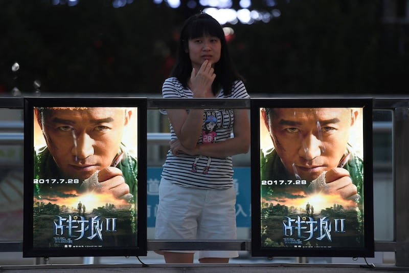 This photo taken on August 7, 2017 shows a woman standing next to movie posters for "Wolf Warriors 2" in Beijing. 
A Chinese action film that depicts the country's soldiers saving war-ravaged Africans from Western baddies soared to become China's all-time top box-office earner on August 8, headlining a summer of patriotic cinematic fare. The wildly popular "Wolf Warriors 2" boasts the ominous tagline "whoever offends China will be hunted down no matter how far away they are", and millions of Chinese cinema-goers have lapped it up since the movie's release less than two weeks ago. / AFP PHOTO / Greg Baker