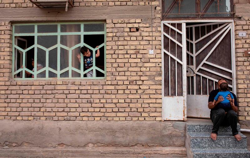 An Iraqi boy looks out of his window at a neighbour sitting with a child on the porch,  amid confinement in the southern city of Basra.  AFP