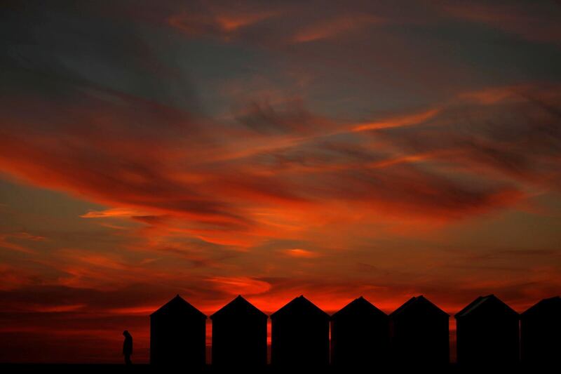 A man enjoys the sunset beside beach cabins on a pebbled beach in Cayeux-sur-Mer, France. Reuters