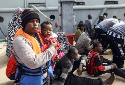 An African migrant carries a child while walking on a dock at the Libyan capital Tripoli's naval base on March 10, 2018, after disembarking following rescue from off the coast of Zawiyah, about 45 kilometres west of the capital. / AFP PHOTO / MAHMUD TURKIA