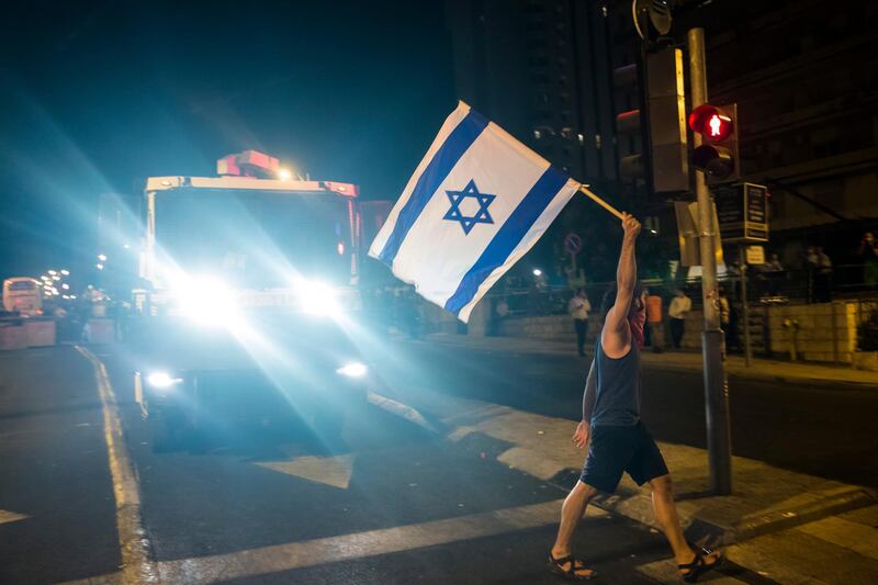 A protester waves the Israeli flag as he walks in front of a police water cannon truck during a demonstration  in Jerusalem. Getty Images