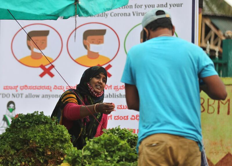 A vegetable seller wearing a face mask around her neck sits in front of a hoarding informing people about proper use of masks in Bengaluru, India.  AP Photo