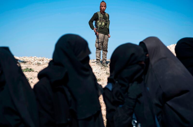 A soldier with the Syrian Democratic Forces keeps watch near veiled women standing on a field after they fled from the Baghouz area in Deir Ezzor. AFP
