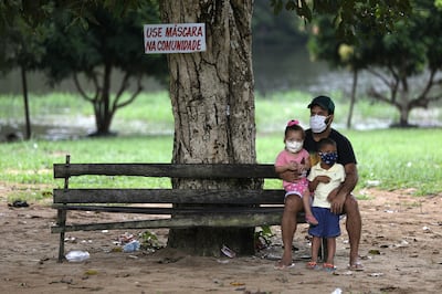 A man with his children are seen next to a sign that reads, "Use mask at the community" at Nossa Senhora do Livramento community, along the Negro river banks.