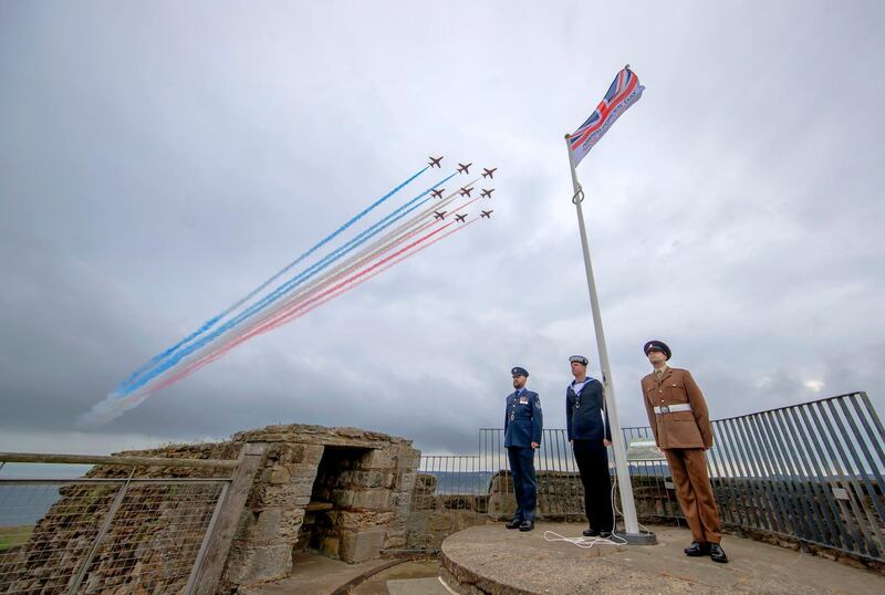 Members of the armed forces stand to attention as the Red Arrows perform a flypast over the grounds of Scarborough Castle where celebrations for Armed Forces Day were due to take place before being cancelled due to coronavirus, in North Yorkshire, England,  Saturday, June 27, 2020. (Danny Lawson/PA via AP)