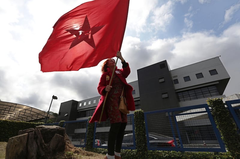 A supporter holds a flag of the Workers' Party in front of the headquarters of the Federal Police where Brazil's former President Luiz Inacio Lula da Silva is jailed for corruption, in Curitiba, Brazil, Tuesday, Sept. 11, 2018. Brazil's Workers' Party replaced da Silva with Fernando Haddad as its presidential candidate for October's general election, clarifying one of the biggest question marks hanging over the vote to lead Latin America's largest nation. (AP Photo/Eraldo Peres)