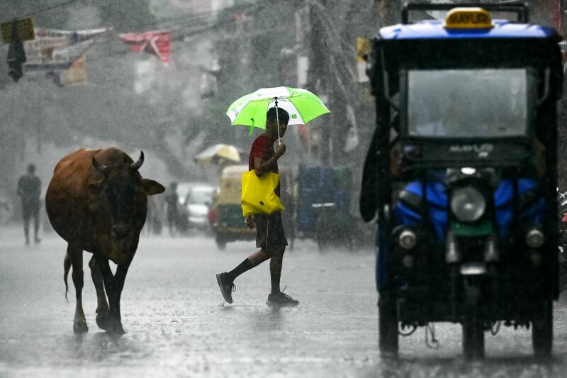 Commuters cross the street during rainfall in New Delhi. AFP