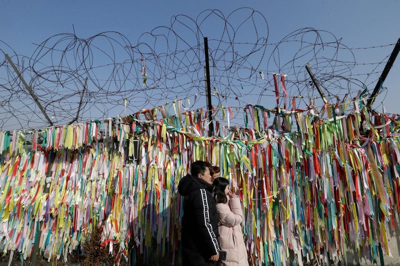 A family pose in front of ribbons placed on a barbed wire fence with messages wishing for the reunification of the country with its neighbour in the north as they visit the border to celebrate the new year at the Imjingak Pavilion in Paju, South Korea. AP Photo