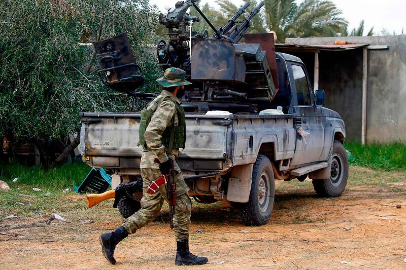 A fighter loyal to the internationally recognised Libyan Government of National Accord (GNA) walks past a vehicle in an area south of the Libyan capital Tripoli on January 12, 2020. Both sides in Libya's conflict agreed to a ceasefire to end nine months of fighting, following weeks of international diplomacy and calls for a truce by power-brokers Russia and Turkey. The UN-recognised Government of National Accord (GNA) in Tripoli had been under attack since last April from forces loyal to eastern-based strongman Khalifa Haftar, which on January 6 captured the strategic coastal city of Sirte. / AFP / Mahmud TURKIA
